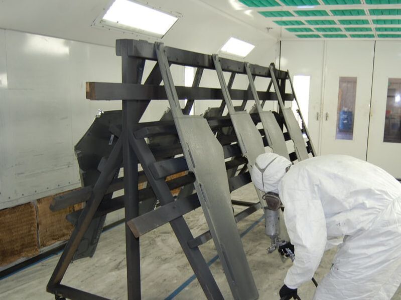 Technician spray-finishing steel parts inside an ICS paint booth